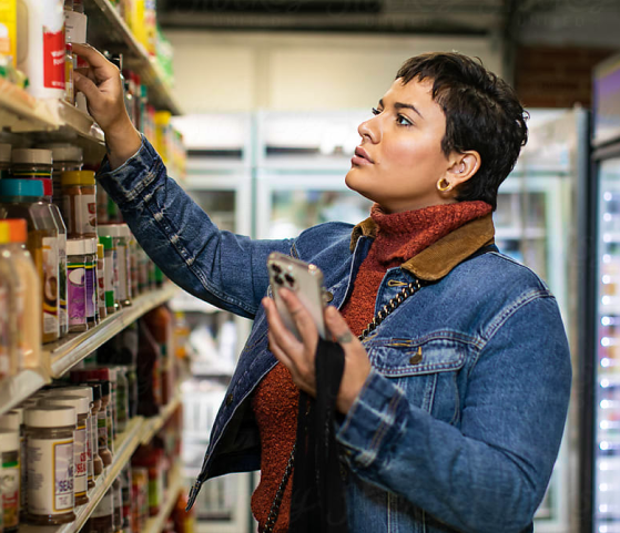 Woman in grocery store aisle reaching for a product on a shelf