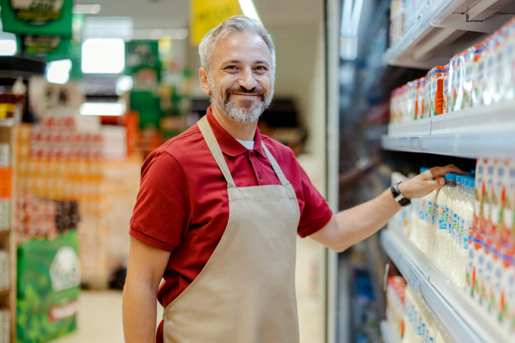 Man in apron smiling in grocery store aisle