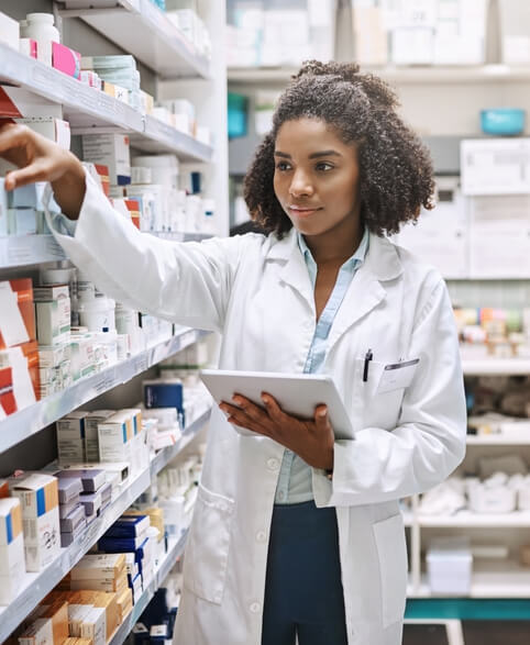 Pharmacist in white coat stocking medicine on shelves