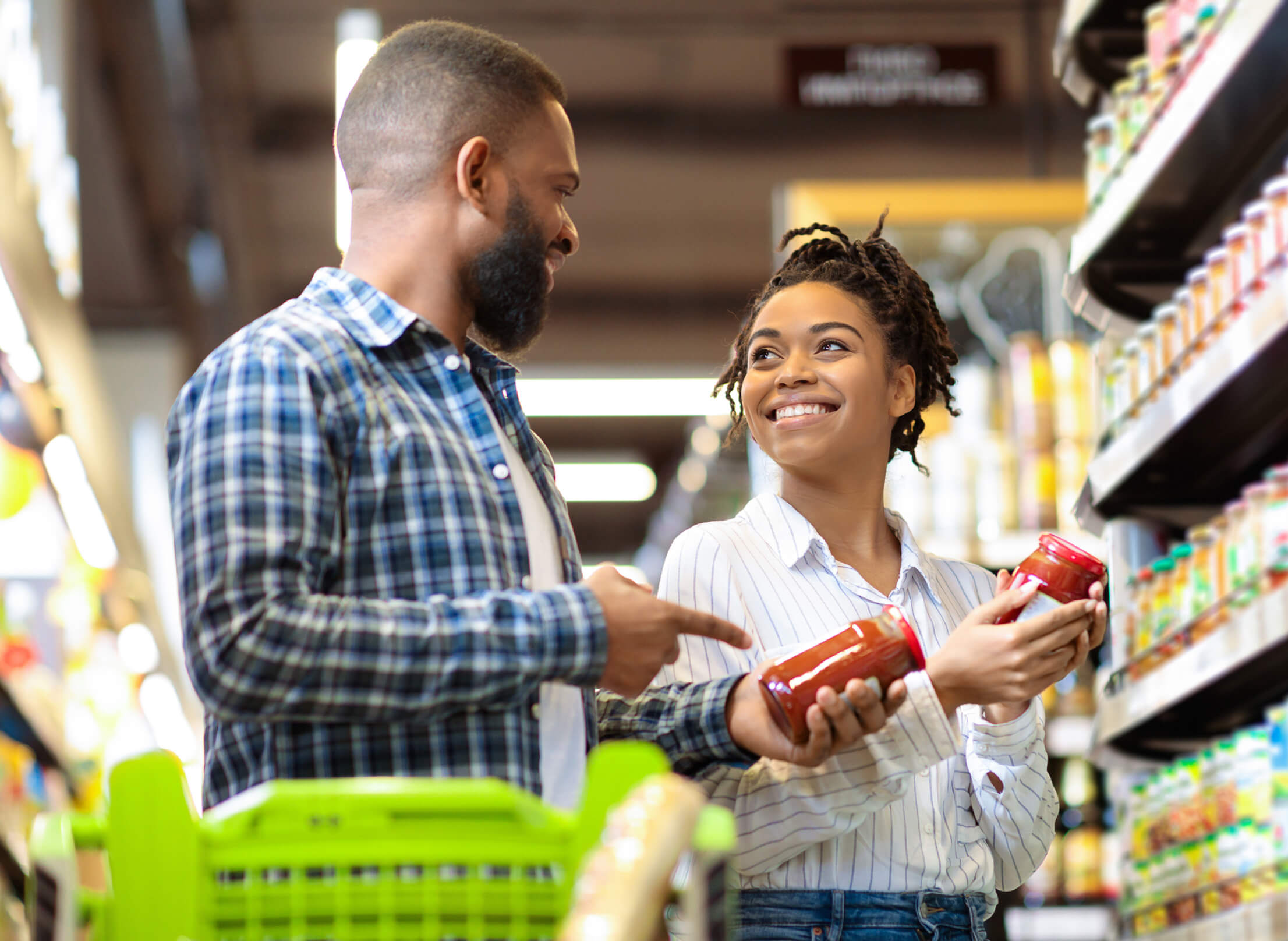 Woman and man shopping in a grocery story and smiling at each other while holding jars of sauce