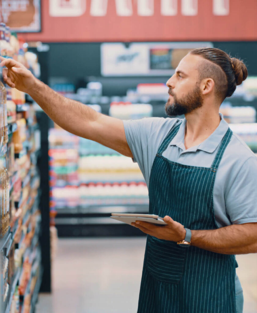 Man with apron looking at products on the shelves in a grocery store aisle