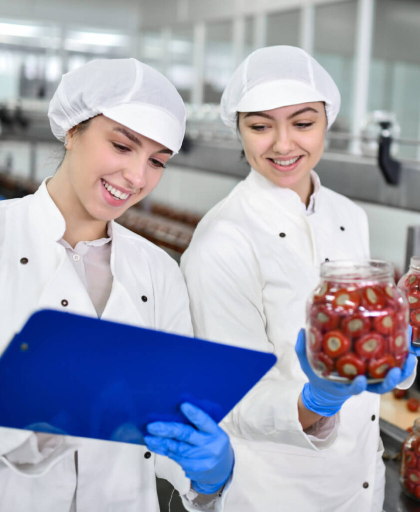 Two women in lab coats, wearing blue latex gloves looking at a clipboard together